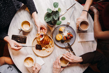 Beleuchtung für eine Cafeteria: Gemütliche Tafel mit Kaffee und frischem Gebäck, umgeben von Gästen.