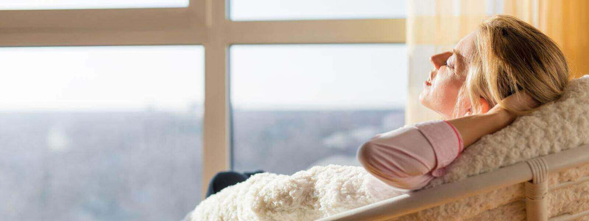 Frau entspannt sich im Sonnenlicht am Fenster und genießt das Wohlbefinden durch natürliches Licht.