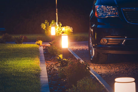 Beleuchtete Einfahrt mit modernen Lampen und einem schwarzen Auto bei Nacht, ideal für sichere Einfahrtsbeleuchtung.