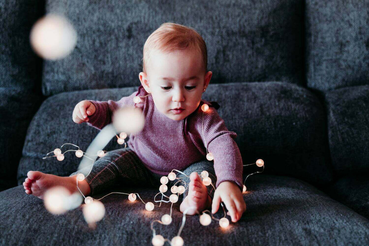 Ein Baby spielt mit Lichtern auf einer Couch, umgeben von warmen, gemütlichen Lichtern in einem behaglichen Raum.