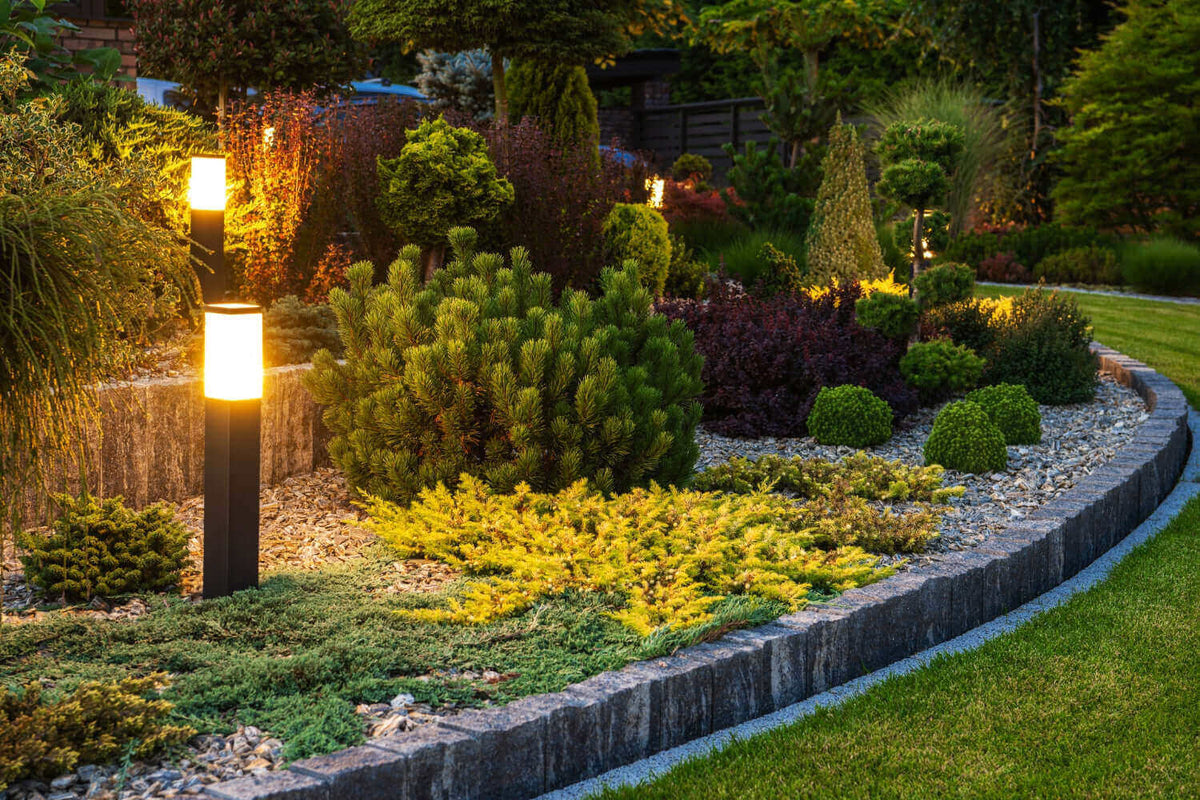 Schöne Gartenbeleuchtung mit modernen Lampen, die Pflanzen und Sträucher in warmem Licht erleuchten.