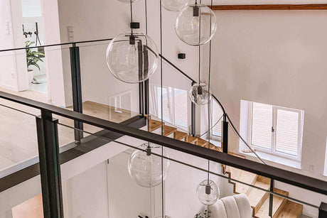 Moderne Galeriebeleuchtung im Treppenhaus mit eleganten Glaskugeln und hellem Holzfußboden.