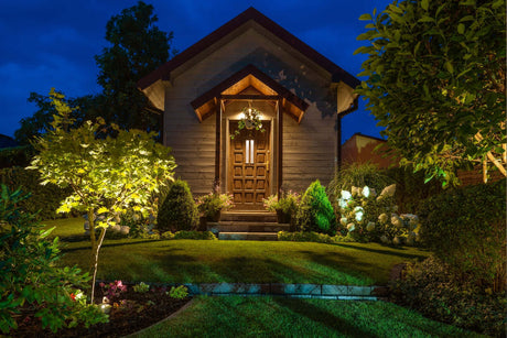Beleuchtetes Gartenhaus bei Nacht mit einladendem Eingang und leuchtenden Pflanzen im Garten.