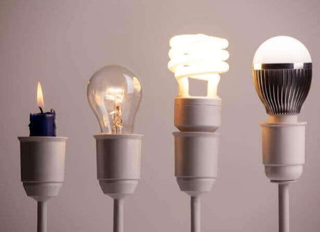 Verschiedene Lichtquellen: Kerze, Glühbirne, Energiesparlampe und LED-Lampe in einem dekorativen Halter.