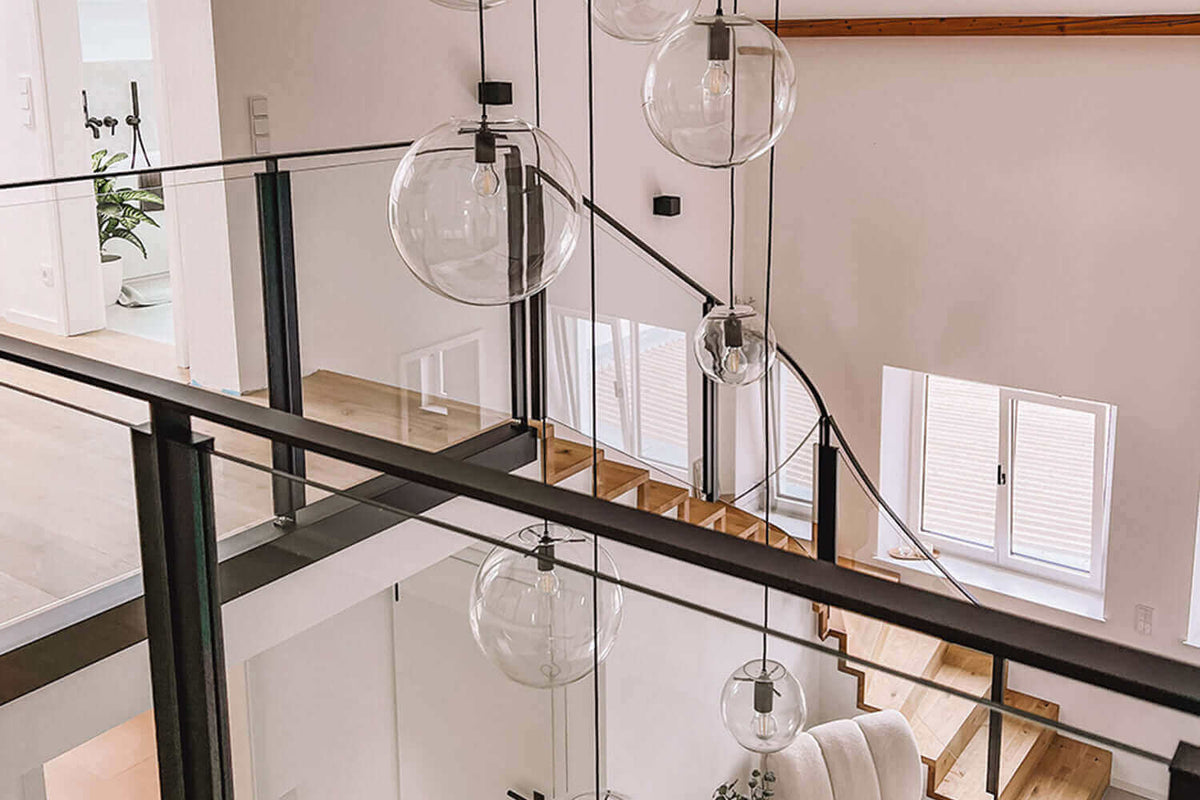 Moderne Galeriebeleuchtung im Treppenhaus mit schlichten, runden Leuchten und elegantem Glasgeländer.