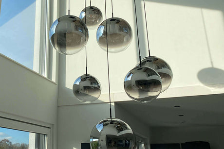 Moderne Pendelleuchten in verschiedenen Größen hängen in einem lichtdurchfluteten Raum.