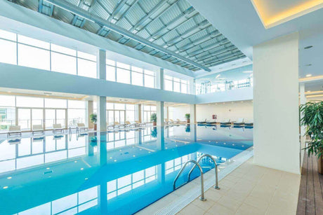 Heller Indoor Pool mit großen Fenstern und modernem Beleuchtungskonzept. Ideale Lichtverhältnisse für Entspannung.