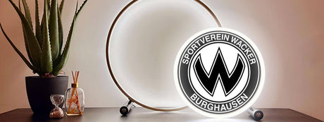Moderne Fußballlampe auf Tisch mit Wacker Burghausen-Logo, umgeben von einer Pflanze und Dekoration.
