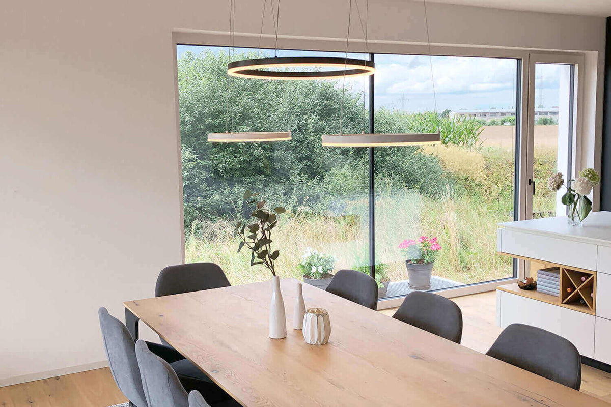 Moderne Esszimmerbeleuchtung mit hängenden Leuchten über einem eleganten Holztisch und Blick auf die Natur.