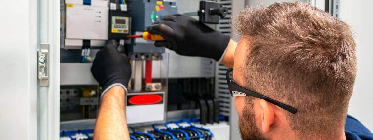 Techniker repariert einen Elektronikschrank mit Schraubendreher, trägt Schutzhandschuhe und Brille.