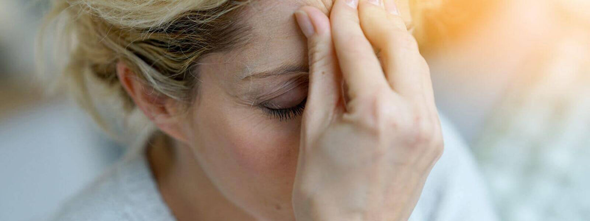 Frau mit Kopfschmerzen, die ihre Stirn hält, symbolisiert schlechte Stimmung und den Bedarf an Lichttherapie.