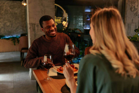 Romantisches Abendessen bei Kerzenschein mit Rotwein und lächelnden Paar in einem stilvollen Restaurant.