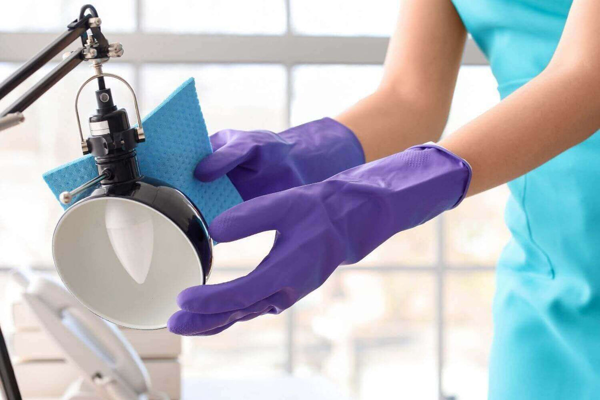 Person mit lila Handschuhen reinigt einen Lampenschirm mit einem blauen Tuch.