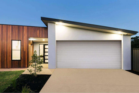 Moderne Garage mit stilvoller Beleuchtung und angelegtem Garten bei Abenddämmerung.