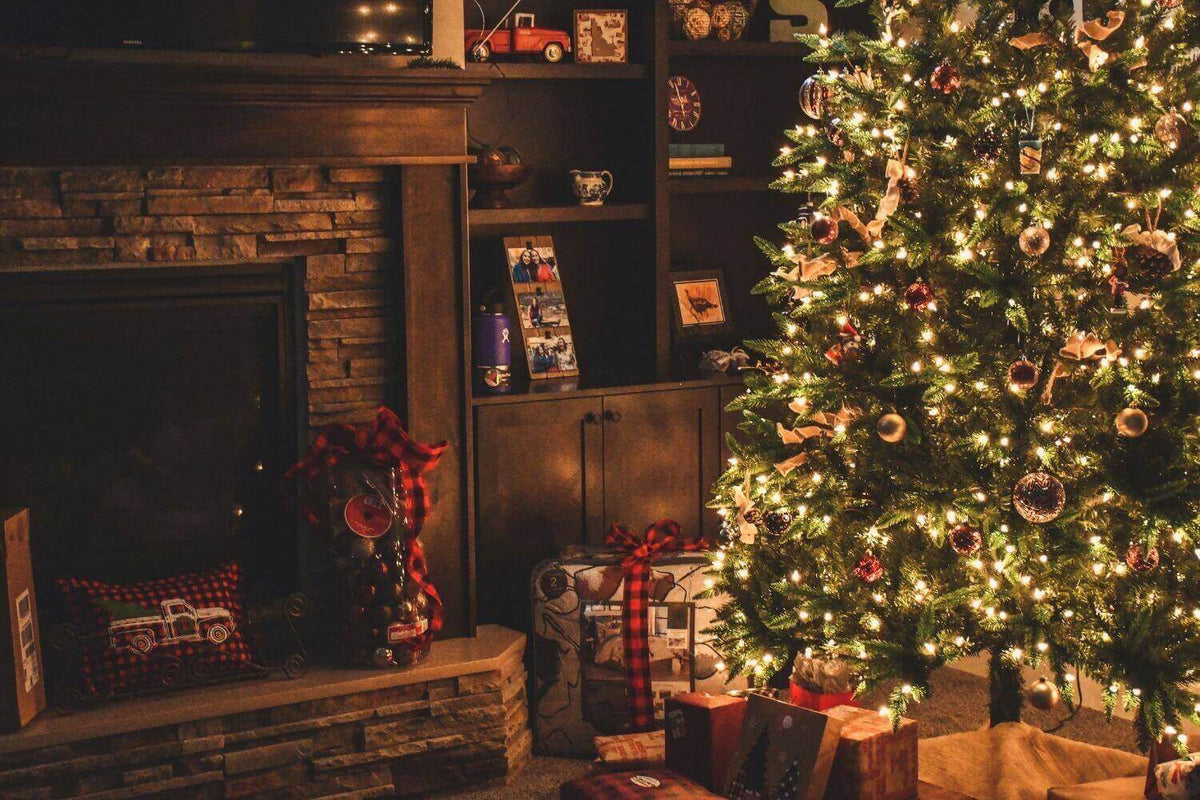 Ein festlich geschmückter Weihnachtsbaum mit Lichtern, Geschenken und einem Kamin im Hintergrund.