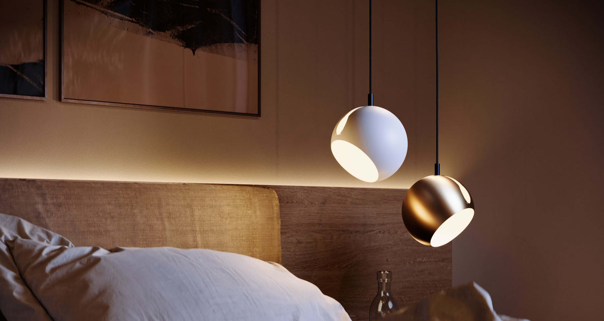 Zwei goldene Hängeleuchten über einem Bett im Schlafzimmer, die warmes Licht ausstrahlen und eine gemütliche Atmosphäre schaffen.