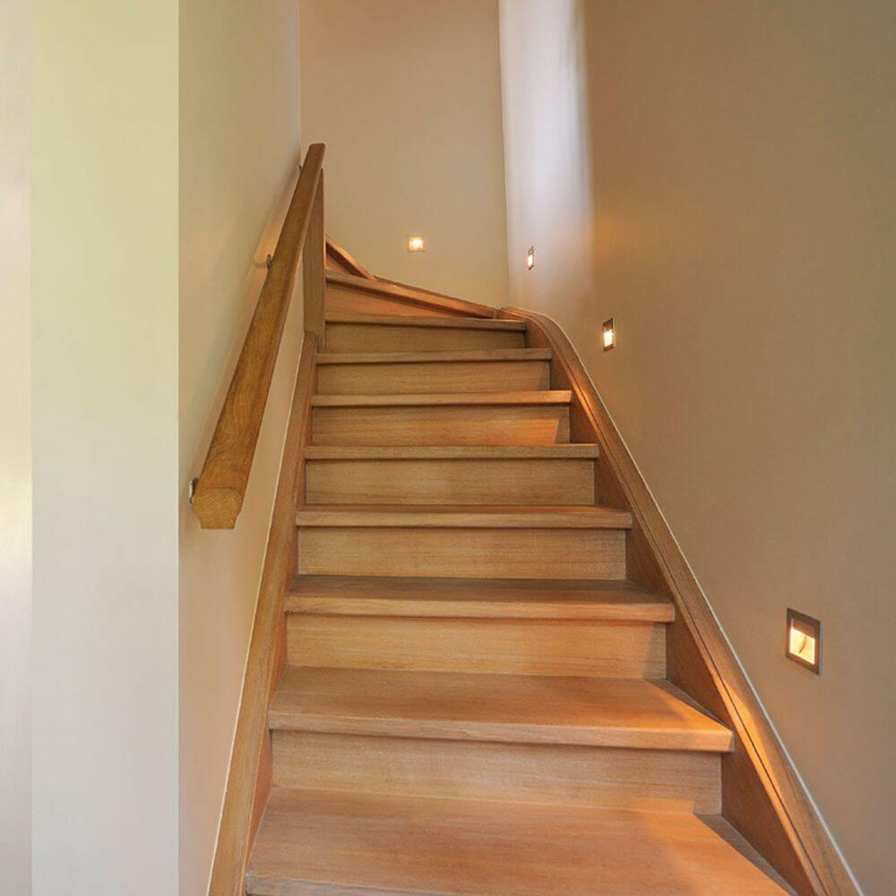 Eingang zu einem hellen Treppenhaus mit stilvollen LED Einbauleuchten und Holzgeländer.