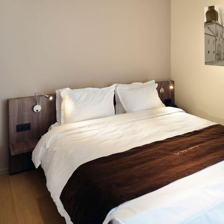 Dio Flaxe Plate wall light chrome GU10 max. 50W above a modern bed in the bedroom area.