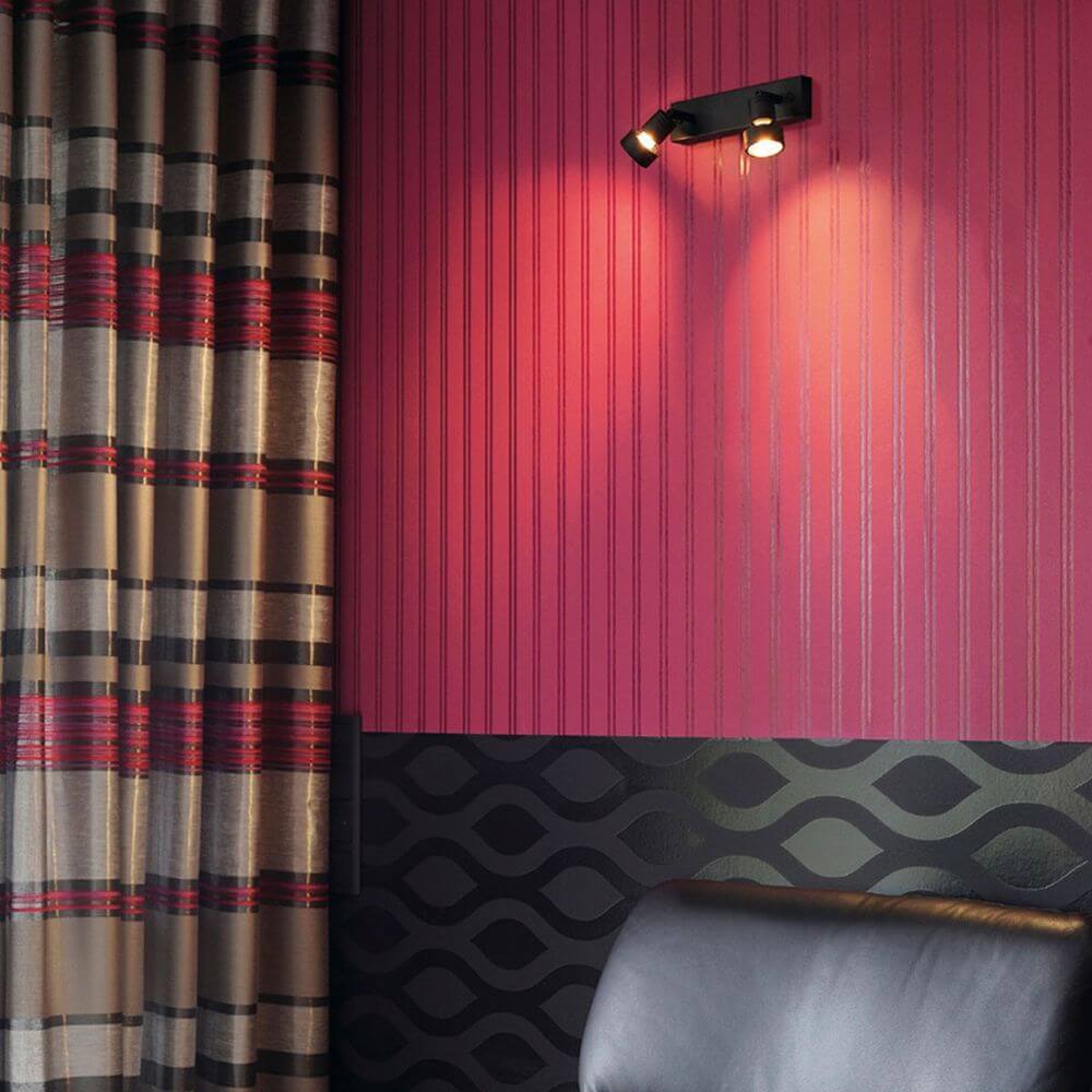 Schwarze Puri 2 Deckenleuchte mit zwei drehbaren Leuchtenköpfen an einer stilvollen Wand mit Rot- und Schwarzmustern.