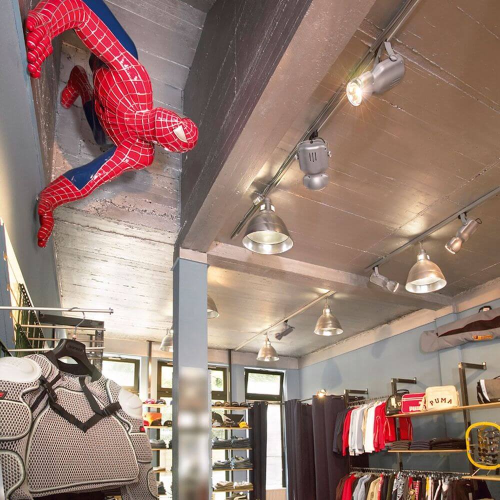 Spiderman Figur klettert an der Decke eines modernen Bekleidungsgeschäfts, beleuchtet von Pendelleuchten.