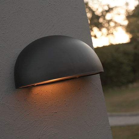 Scorpius Maxi udendørs væglampe sort på en væg i udendørsområdet med varmt lys.
