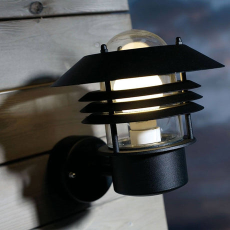 Vejers utendørs vegglampe i svart med lampeskjerm rettet oppover, montert på en trevegg.