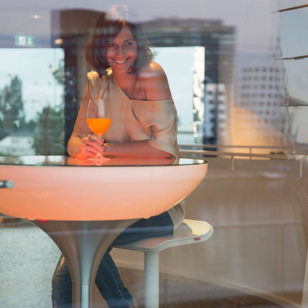Moree Barhocker Ed höhenverstellbar Anthrazit, moderne Frau mit Cocktail am Tisch, stilvolles Ambiente.