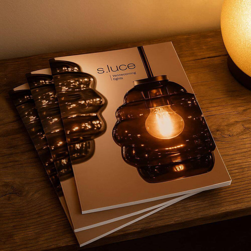 s.luce Katalog mit stilvollen Leuchten auf einem Holztisch mit sanftem Licht im Hintergrund.