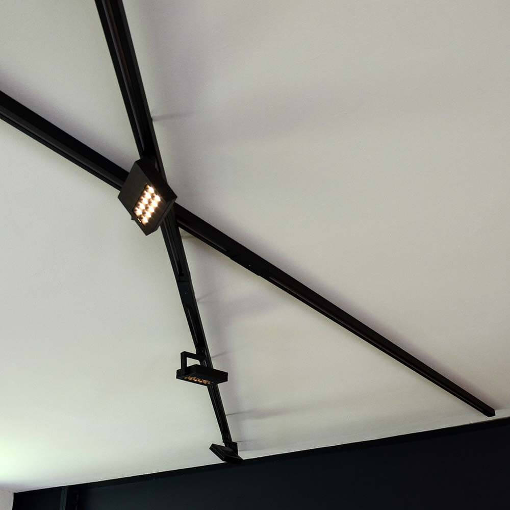 3-Phasen Mittel-Einspeiser Schwarz installiert auf einer Decke mit modernen Lichtschienen.