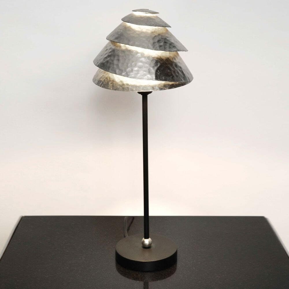 Tischleuchte Snail One Eisen Schwarz-Silber mit metallischem Lampenschirm auf schwarzem Untergrund.