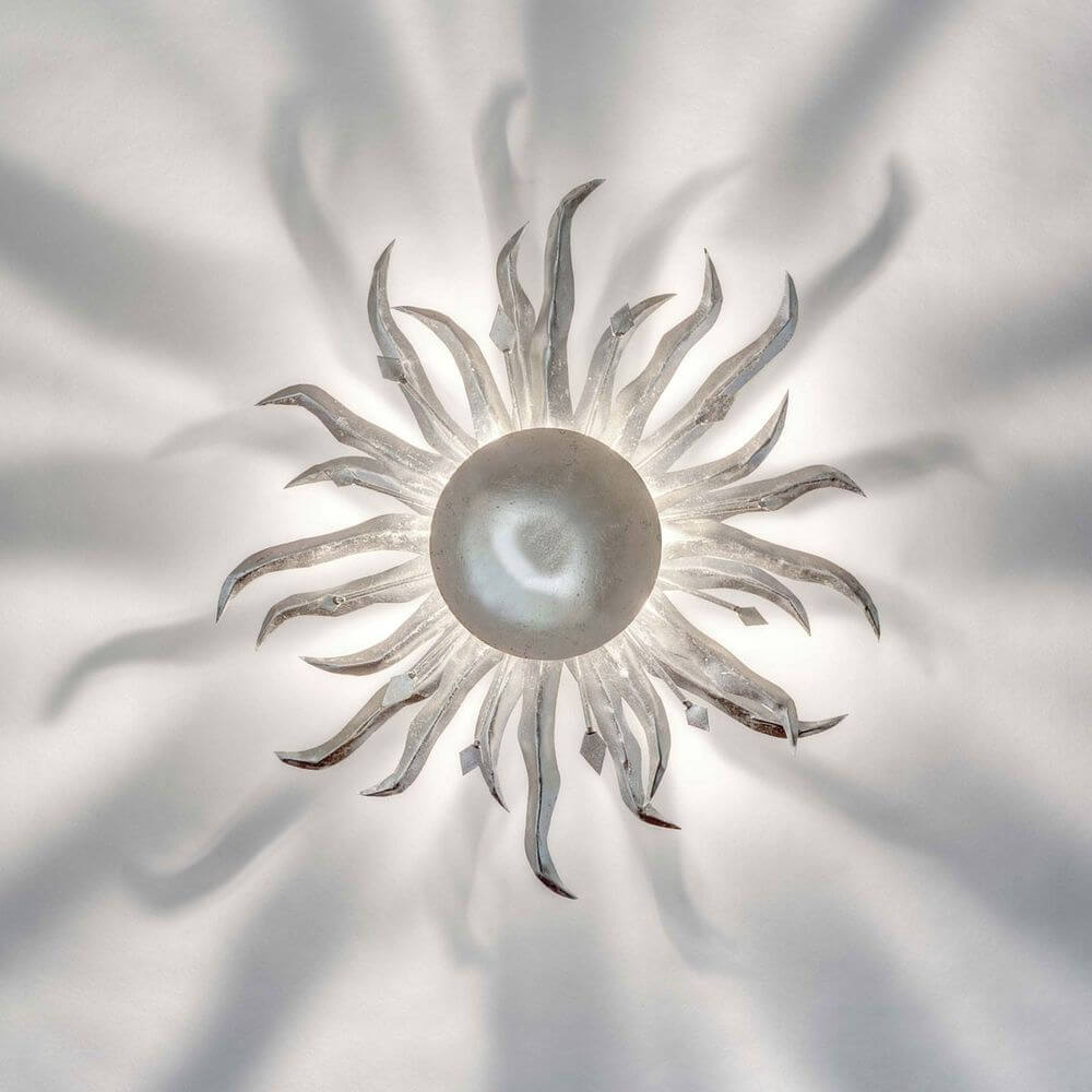 Wandleuchte Sonne Piccola Eisen Silber mit strahlenden Lichtmustern an der Wand.