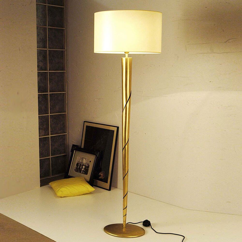 Innovazione gulvlampe i jern og gull med et elegant gyllent design og hvit lampeskjerm på et bord.