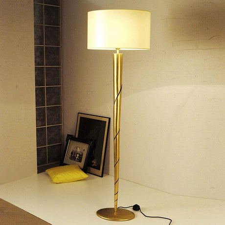 Candeeiro de pé Innovazione ferro dourado com um elegante design dourado e um abajur branco sobre uma mesa.