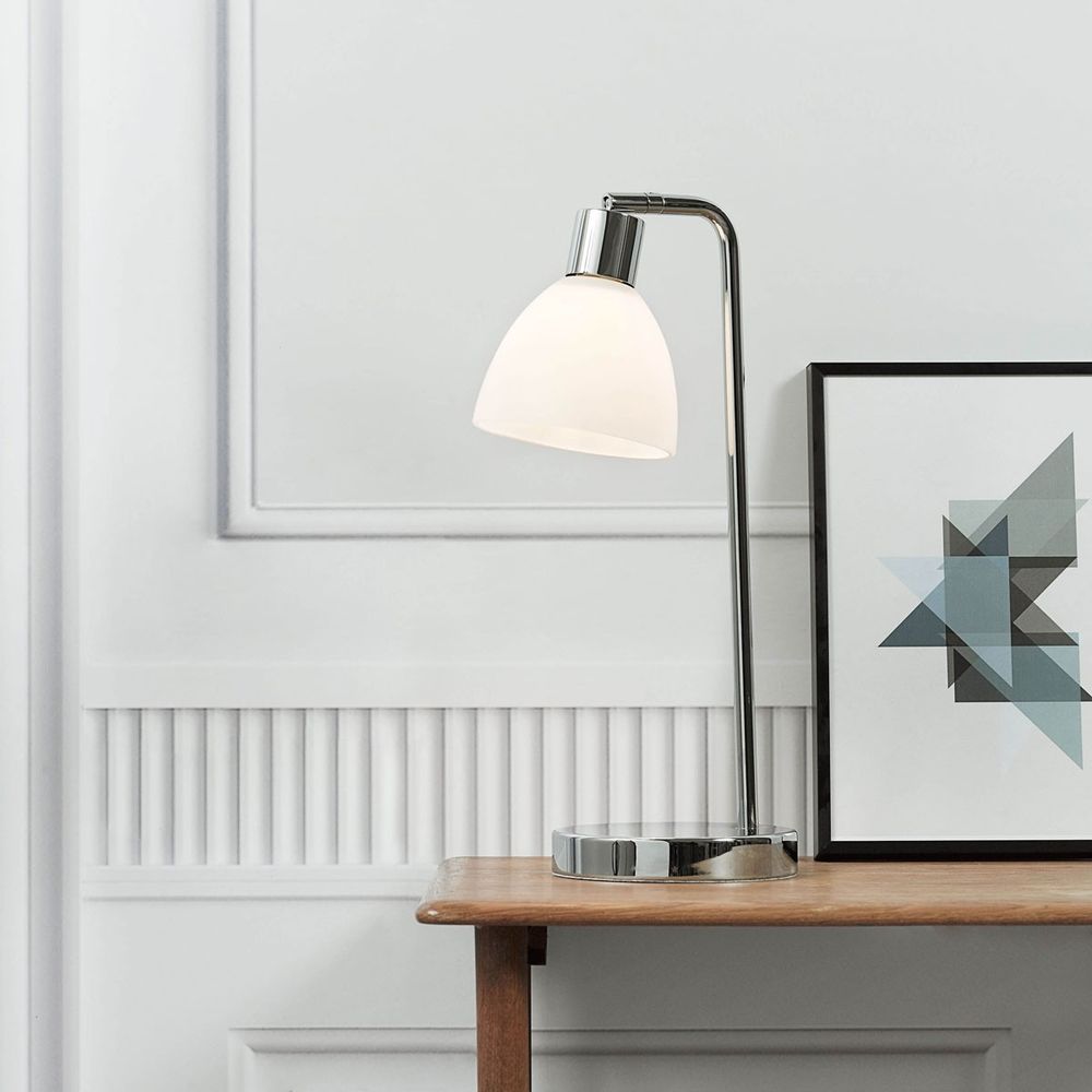 Lampe de table Ray en chrome avec un abat-jour en verre sur une table en bois, idéale pour un aménagement intérieur élégant.