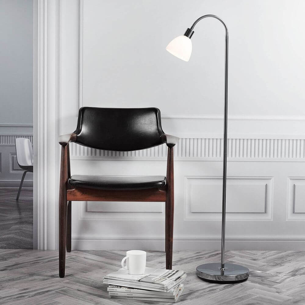 Ray Stehlampe 152 Chrom neben einem Holzstuhl in einem stilvollen Raum mit Tageslicht.
