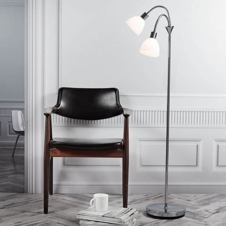 Lampada da terra Ray cromata accanto a una sedia in legno, design elegante con paralumi in vetro.