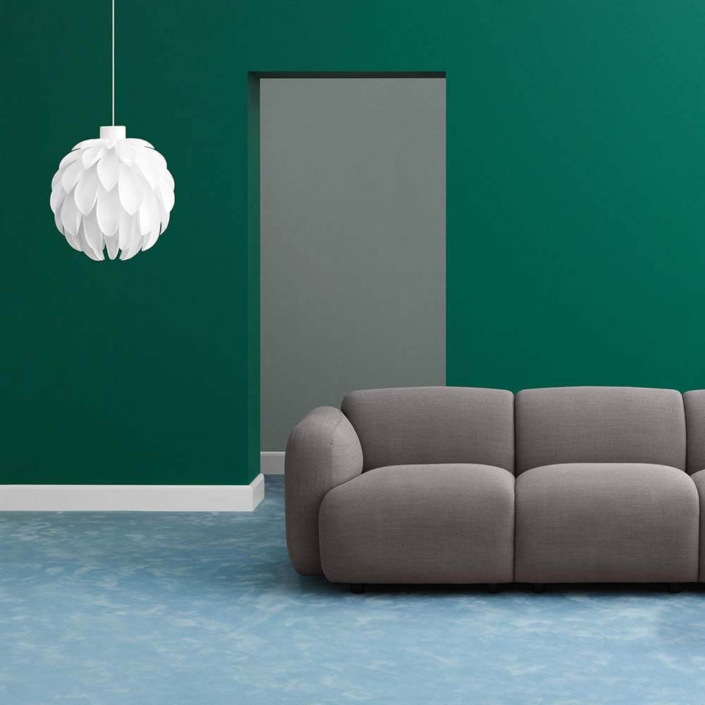 Abgerundete Pendelleuchte Norm12 XL Weiß in einem modernen Wohnraum mit grauem Sofa und grünem Wandanstrich.