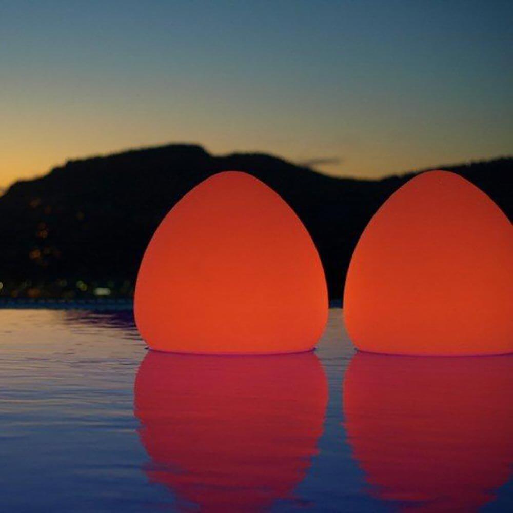 Zwei leuchtende Akku LED-Außenlampen Stone XL in orange am Pool mit Bergkulisse im Hintergrund.