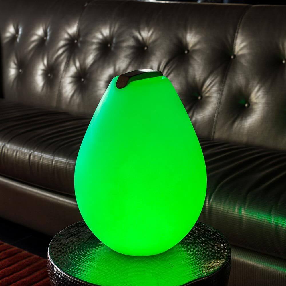 Akku LED-Dekolampe Vessel S in grün leuchtend auf einem Tisch neben einem Ledersofa.