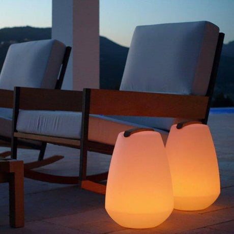 Akumulatorowa LED lampa dekoracyjna Vessel S z drewnianym uchwytem i sterowaniem za pomocą aplikacji obok przytulnego fotela w przestrzeni zewnętrznej.