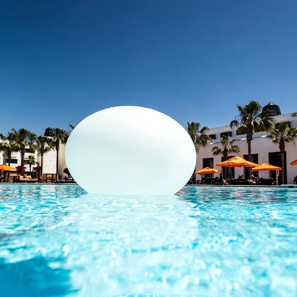 Akku LED-Designleuchte Flatball schwimmend im Pool mit klarem blauen Wasser und Sonnenschein.