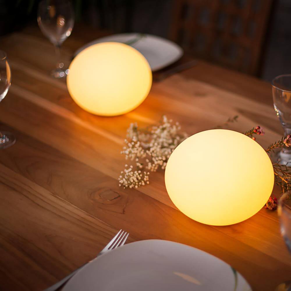 Zwei leuchtende Akku LED-Designleuchten Flatball auf einem Holztisch, ideal für Garten und Terrasse.