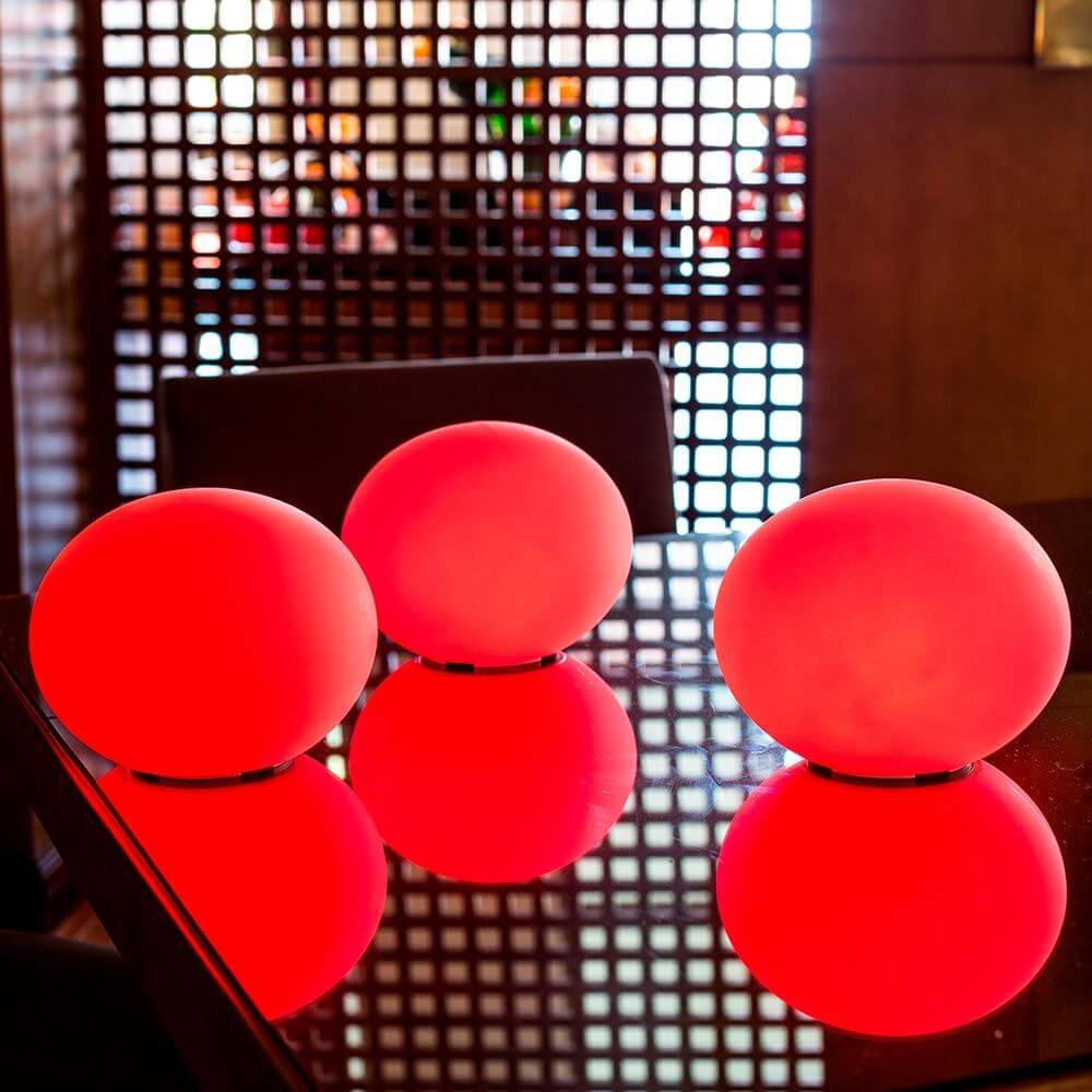 Akku LED-Designleuchte Flatball in Rot, drei Leuchten auf einem Tisch reflektieren Licht in modernem Ambiente.