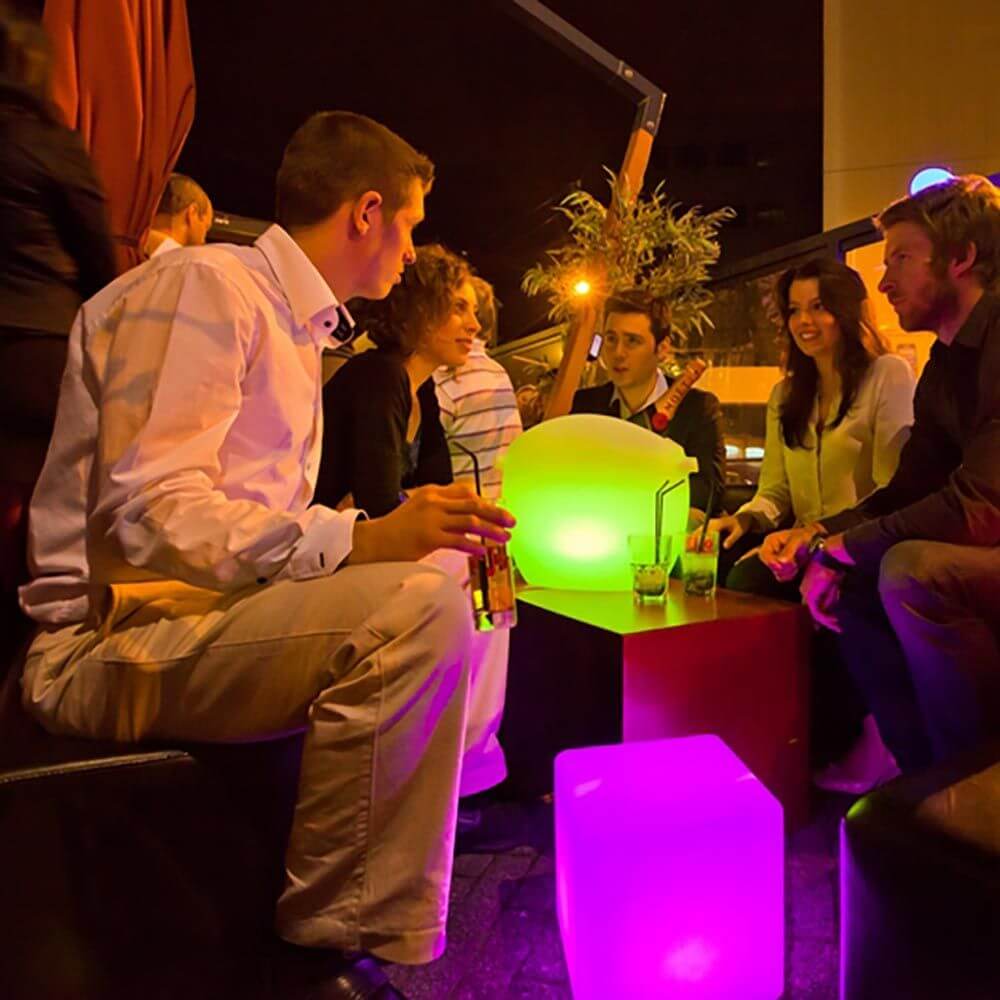 Gruppe von Freundinnen und Freunden in einer modernen Bar, umgeben von bunten LED-Möbeln und Getränken.