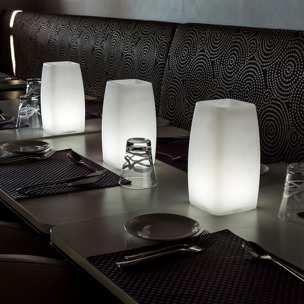 Akku LED-Tischlampe Stele mit App-Steuerung auf einem Restauranttisch mit eleganten Geschirr und Besteck.