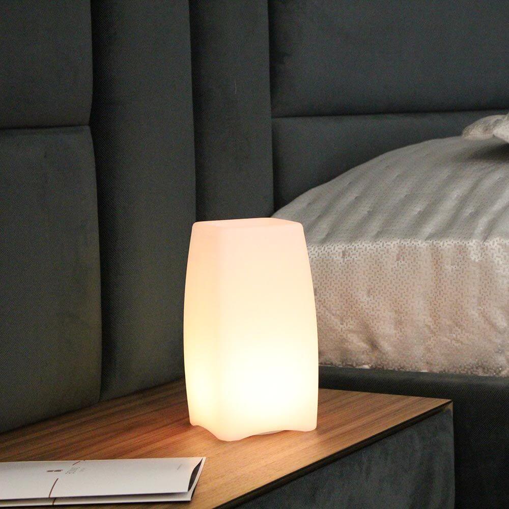 Akku LED-Tischlampe Stele mit App-Steuerung auf einem Nachttisch, warmes Licht, modernes Design.