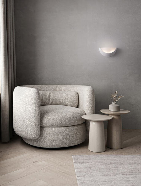 Alas wall light E14 above a modern, round, light armchair and minimalist side tables in a grey room.