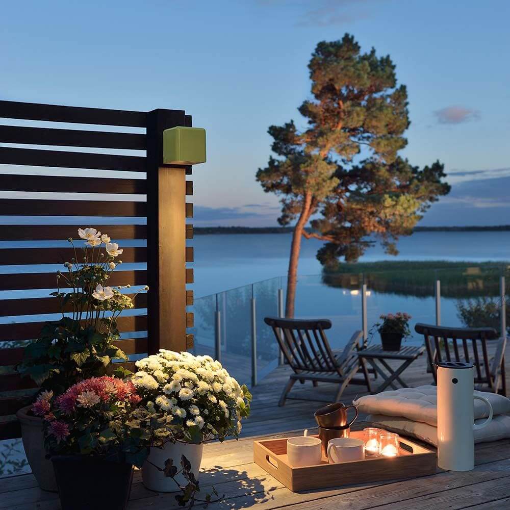 Amalfi LED Außen-Wandleuchte in Oliv, elegant illuminiert Terrasse mit Blumen und Blick auf See bei Dämmerung.