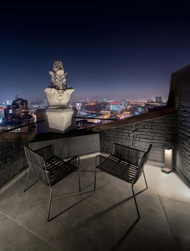 Gemütlicher Balkon mit zwei Stühlen und schöner Aussicht auf die Stadt bei Nacht.