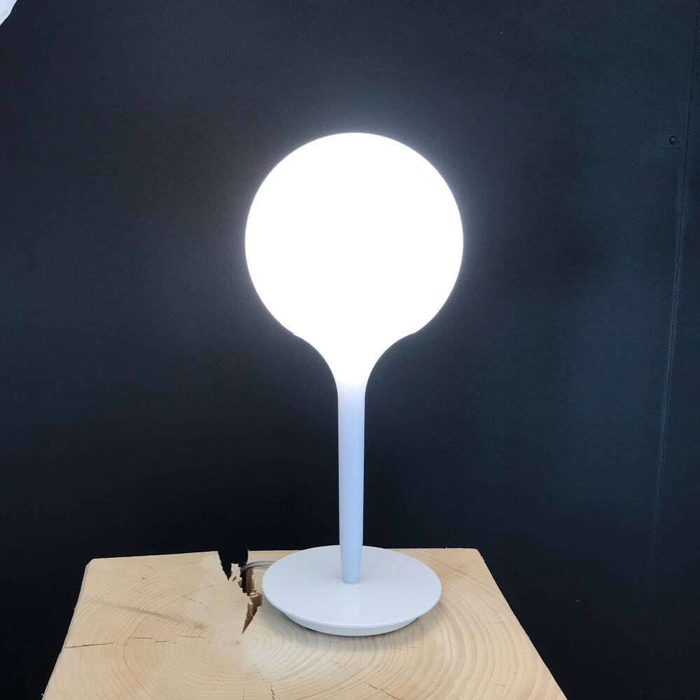 Artemide Castore Tischleuchte mit runder, weißer Glaskugel und modernem Design auf Holzuntergrund.